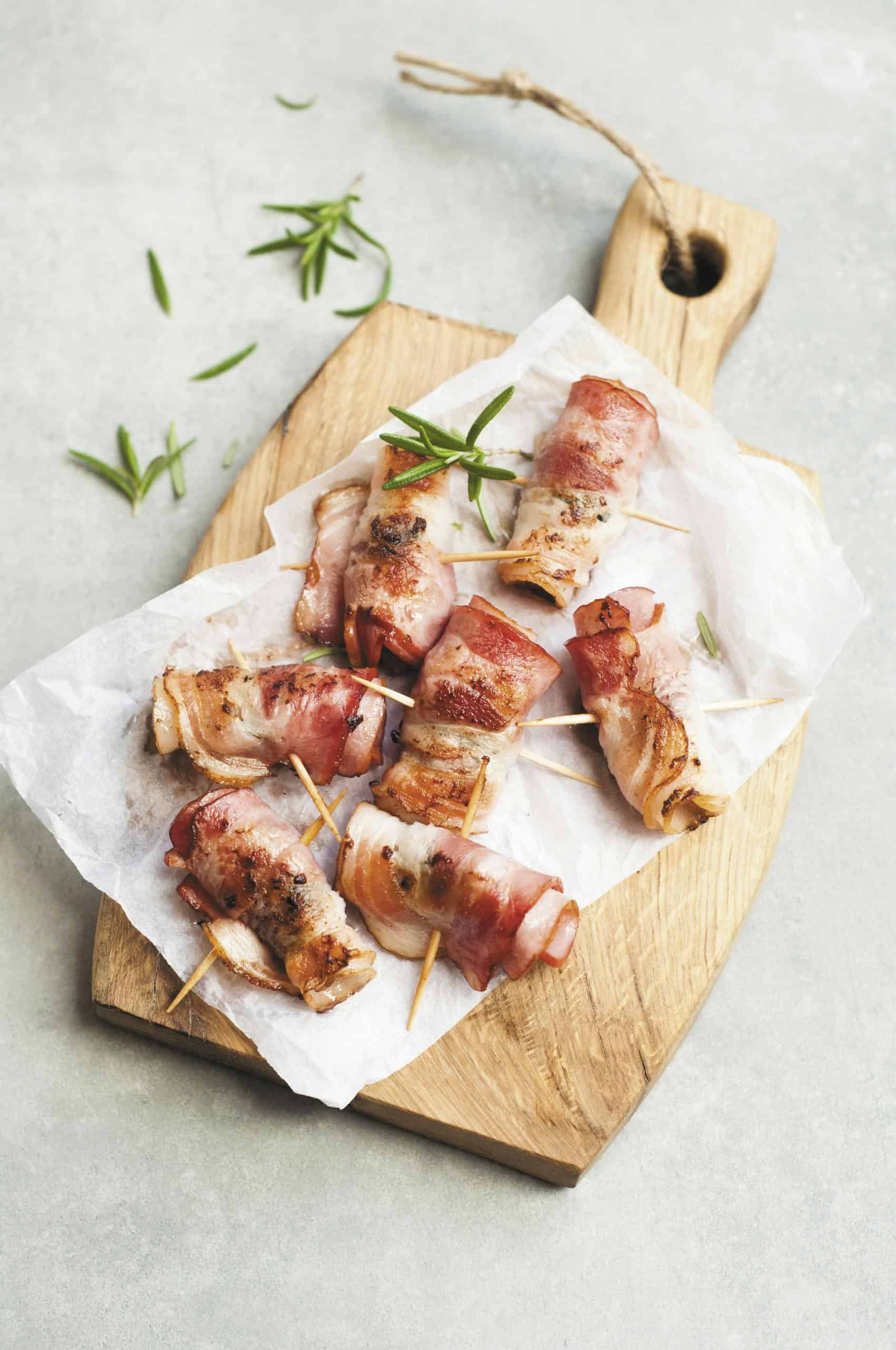 Delicious bacon wrapped chicken bites on a wooden board with herbs, perfect for a savory appetizer.