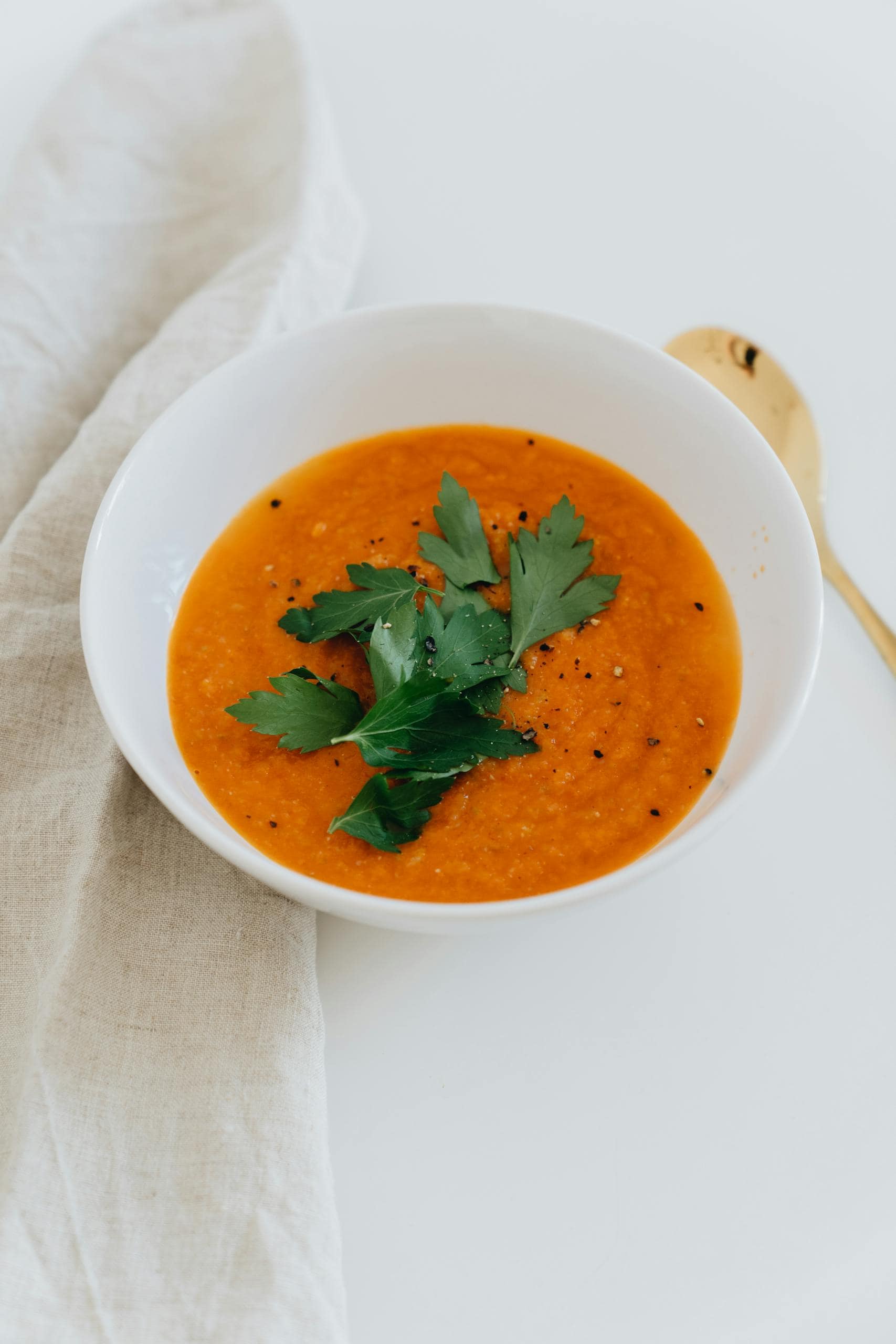 Delicious homemade tomato soup garnished with fresh parsley leaves in a white bowl on a clean background.