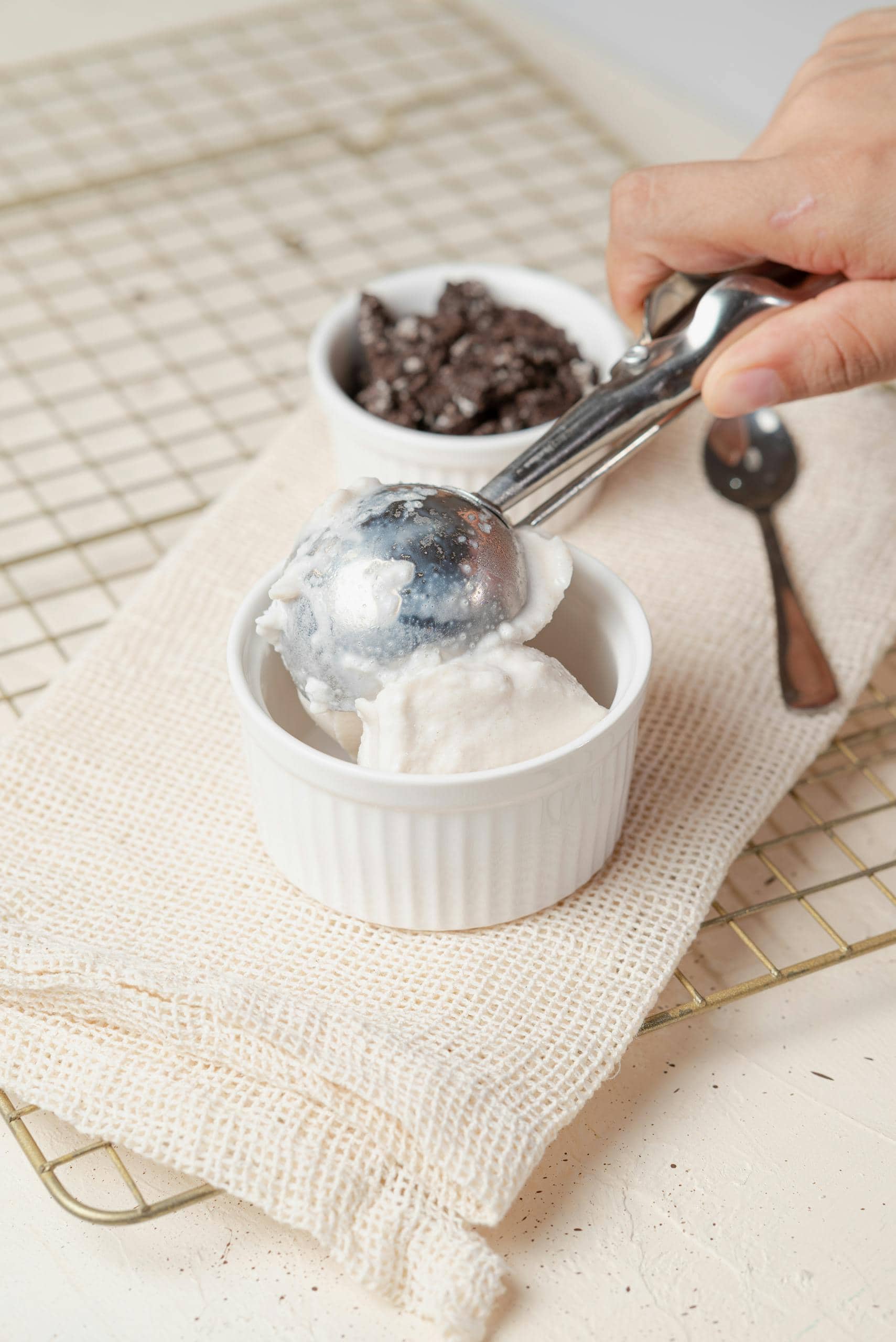Hand scooping vanilla ice cream with chocolate crumble topping on a white napkin.