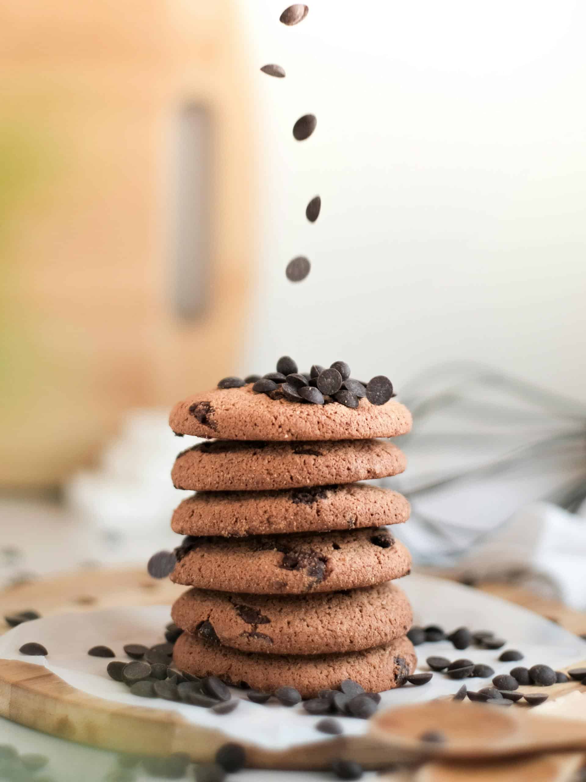 Stack of chocolate chip cookies with chocolate chips falling from above, perfect snack display.