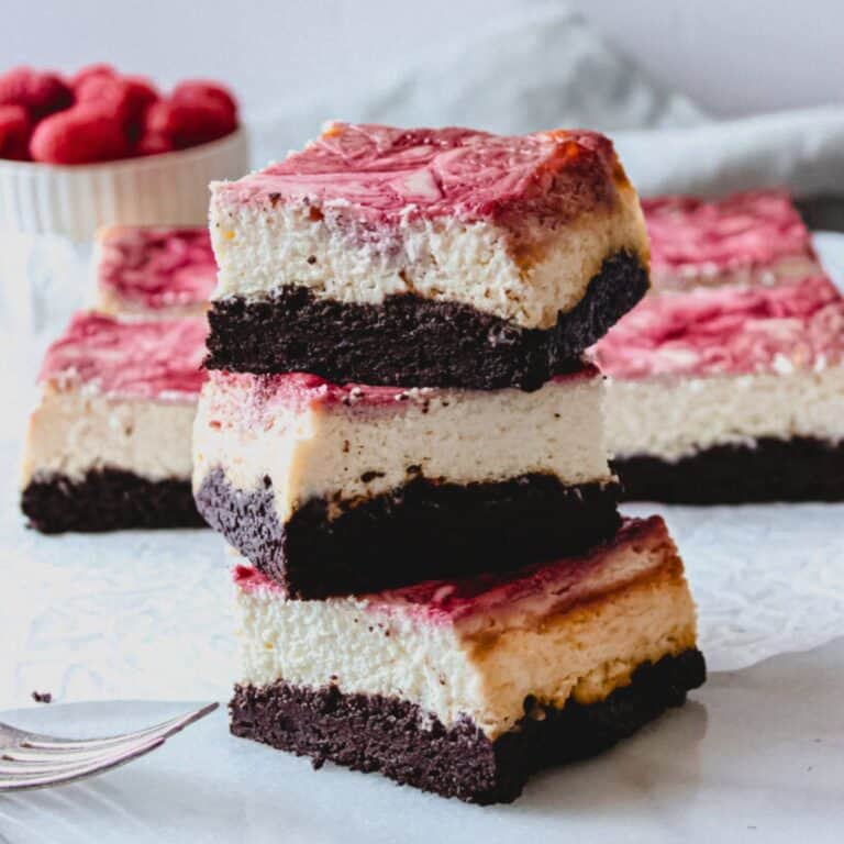 Raspberry cheesecake brownie bars stacked over a marble surface