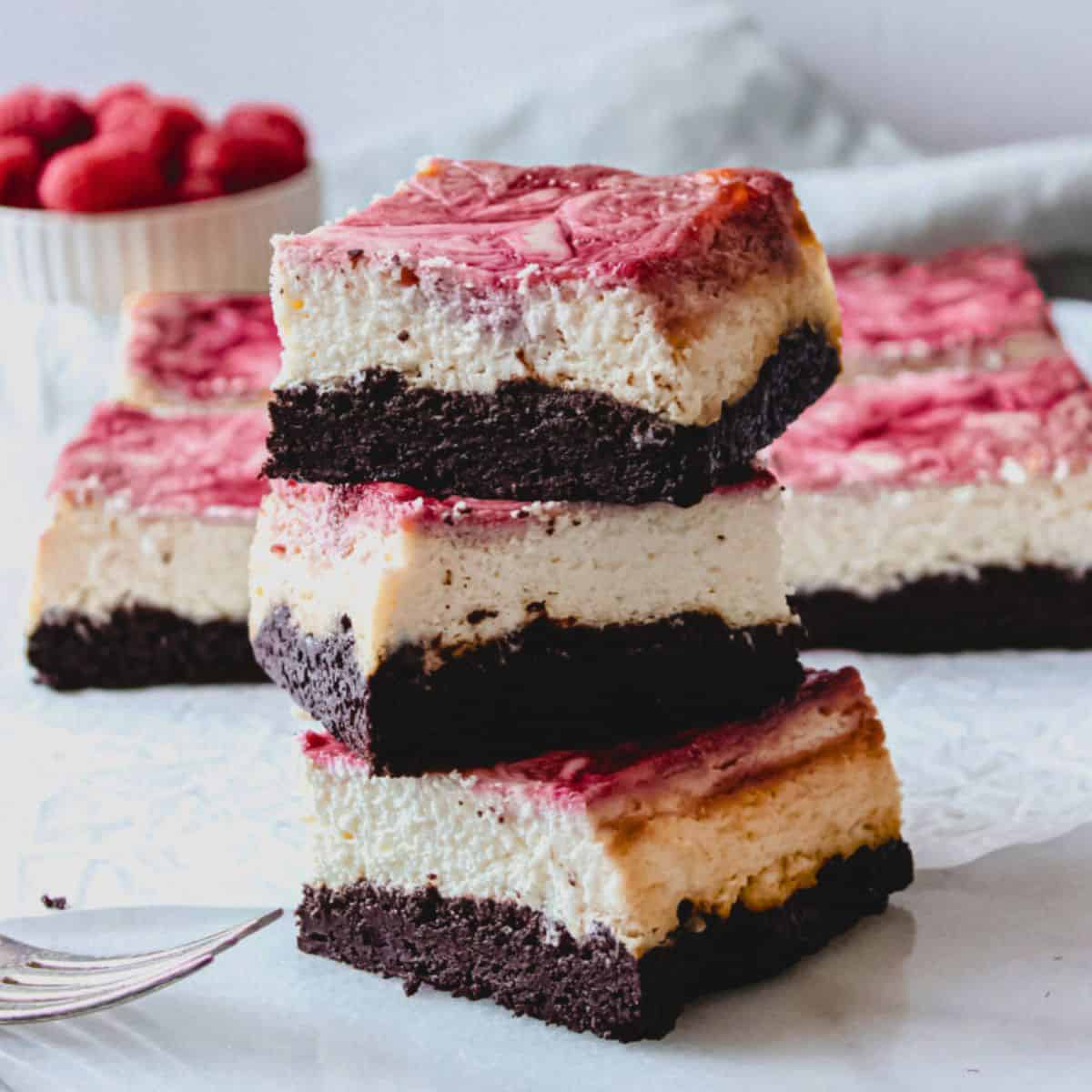 Raspberry cheesecake brownie bars stacked over a marble surface