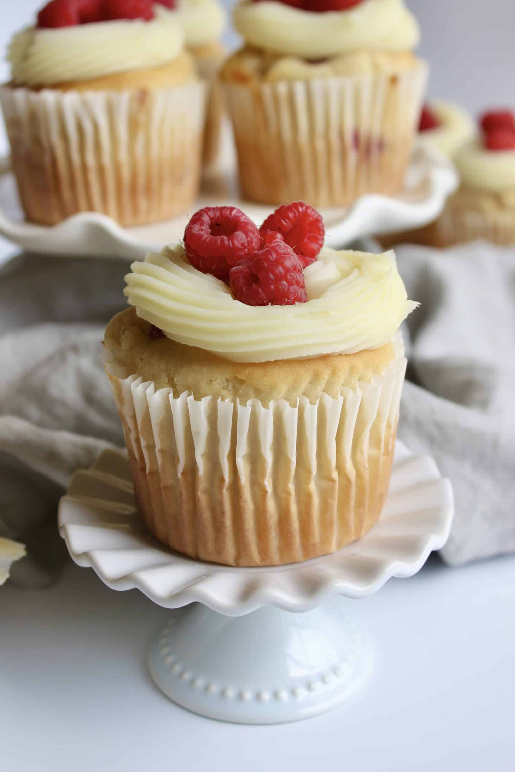 Raspberry cupcakes with white chocolate ganache and garnished with fresh raspberries.