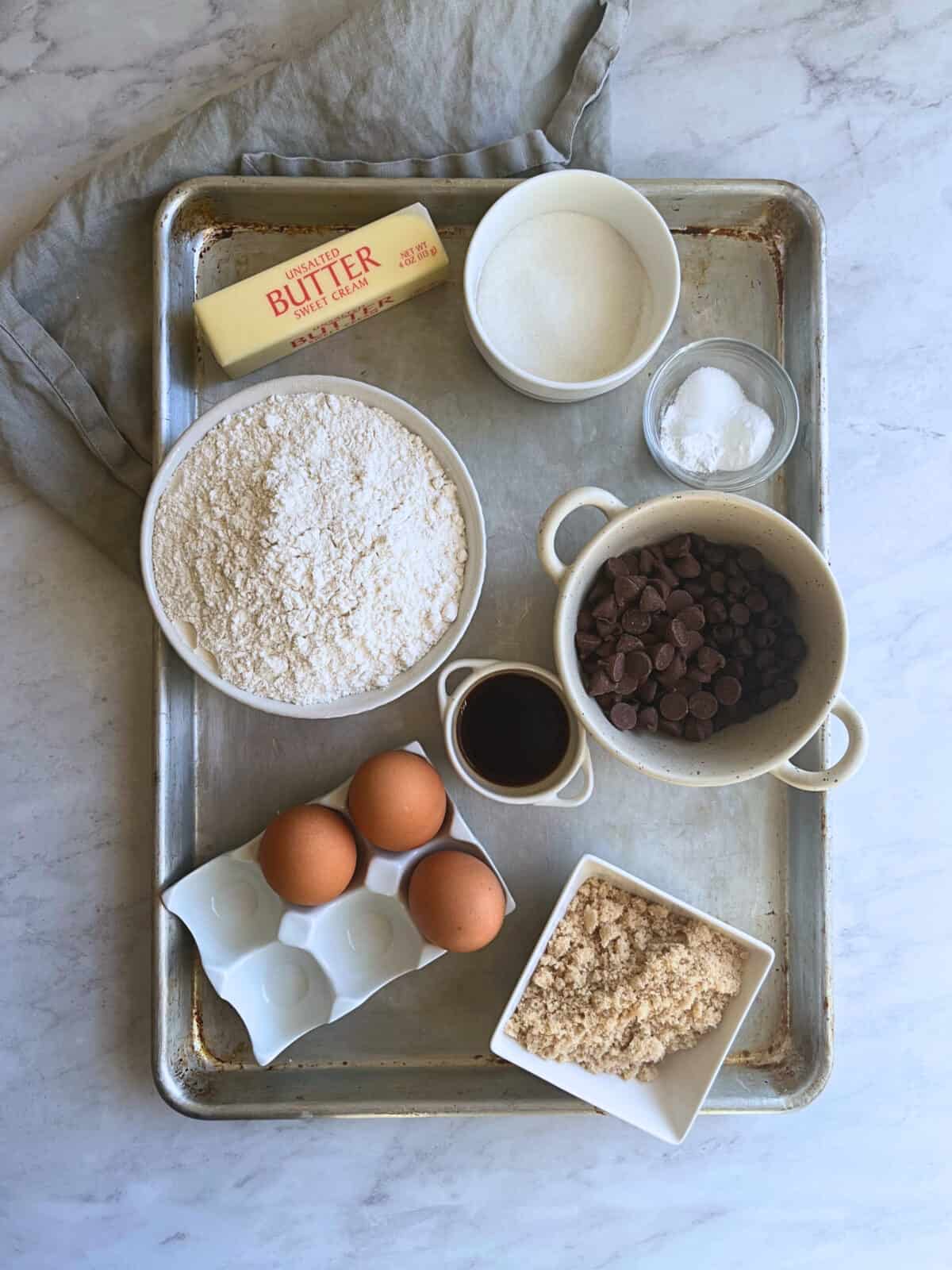 Flat flay of chocolate chip cookie ingredients portioned in bowls over a baking tray