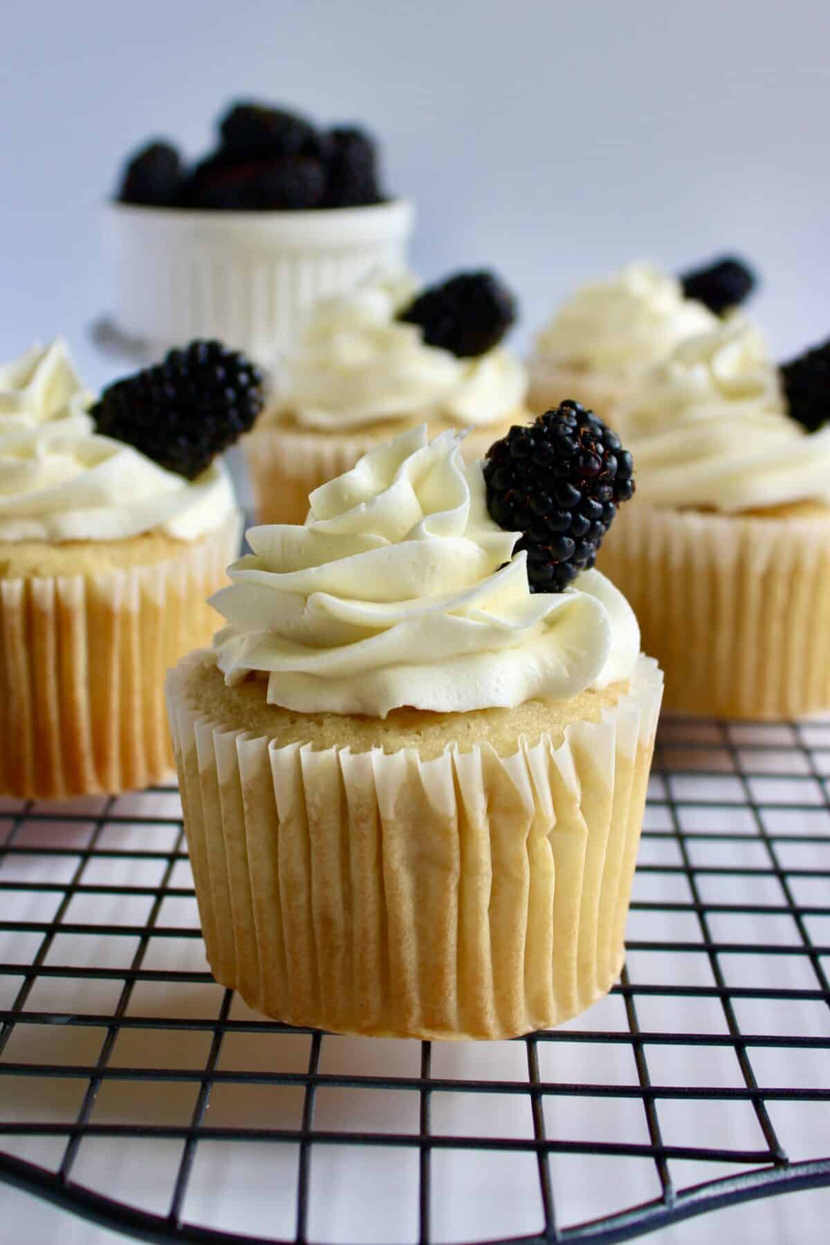 Lemon blackberry cupcakes laid on top of a cooling rack over a white background.