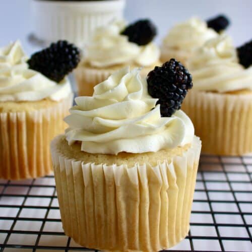 Lemon blackberry cupcakes laid on top of a cooling rack over a white background.