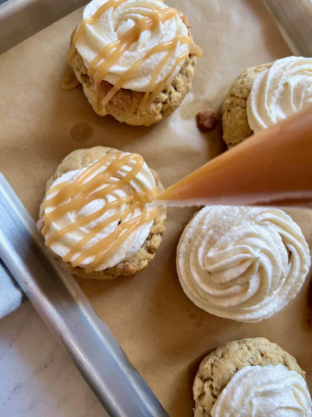 Apple cookies topped with frosting swirls and caramel drizzle on a cooling rack.