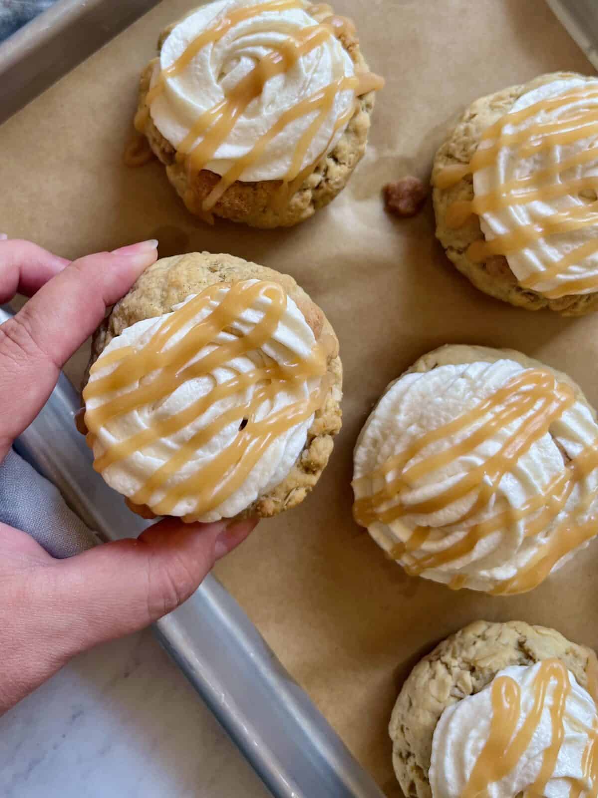 Hands picking a caramel drizzled apple cookie