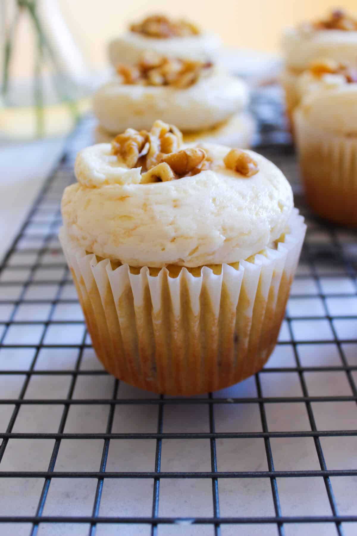 Frosted pear cupcakes on a cooling rack with chopped walnuts sprinkled on top.